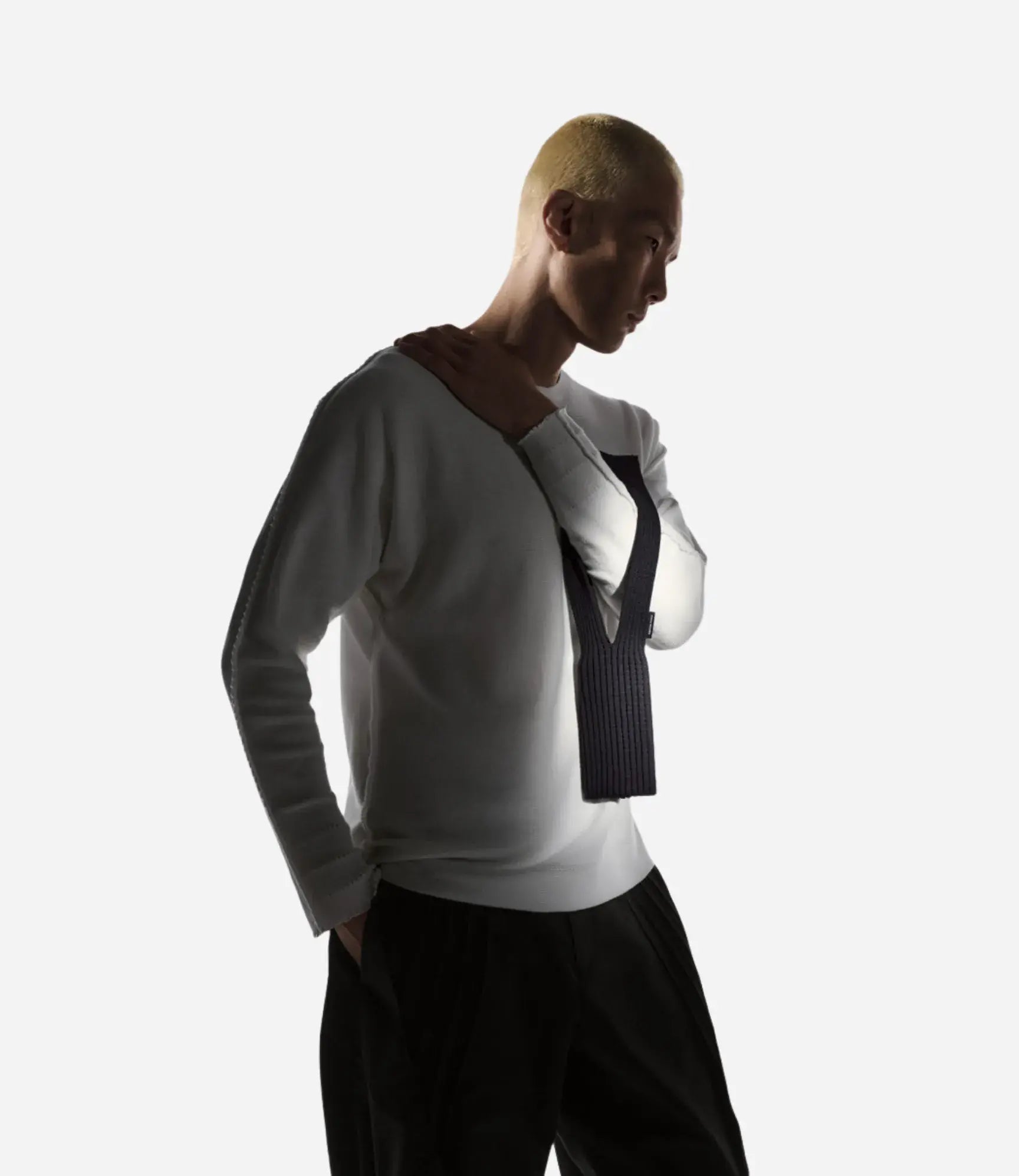 Person wearing a white long-sleeve top with a black vest over a white shirt, standing against a white background.